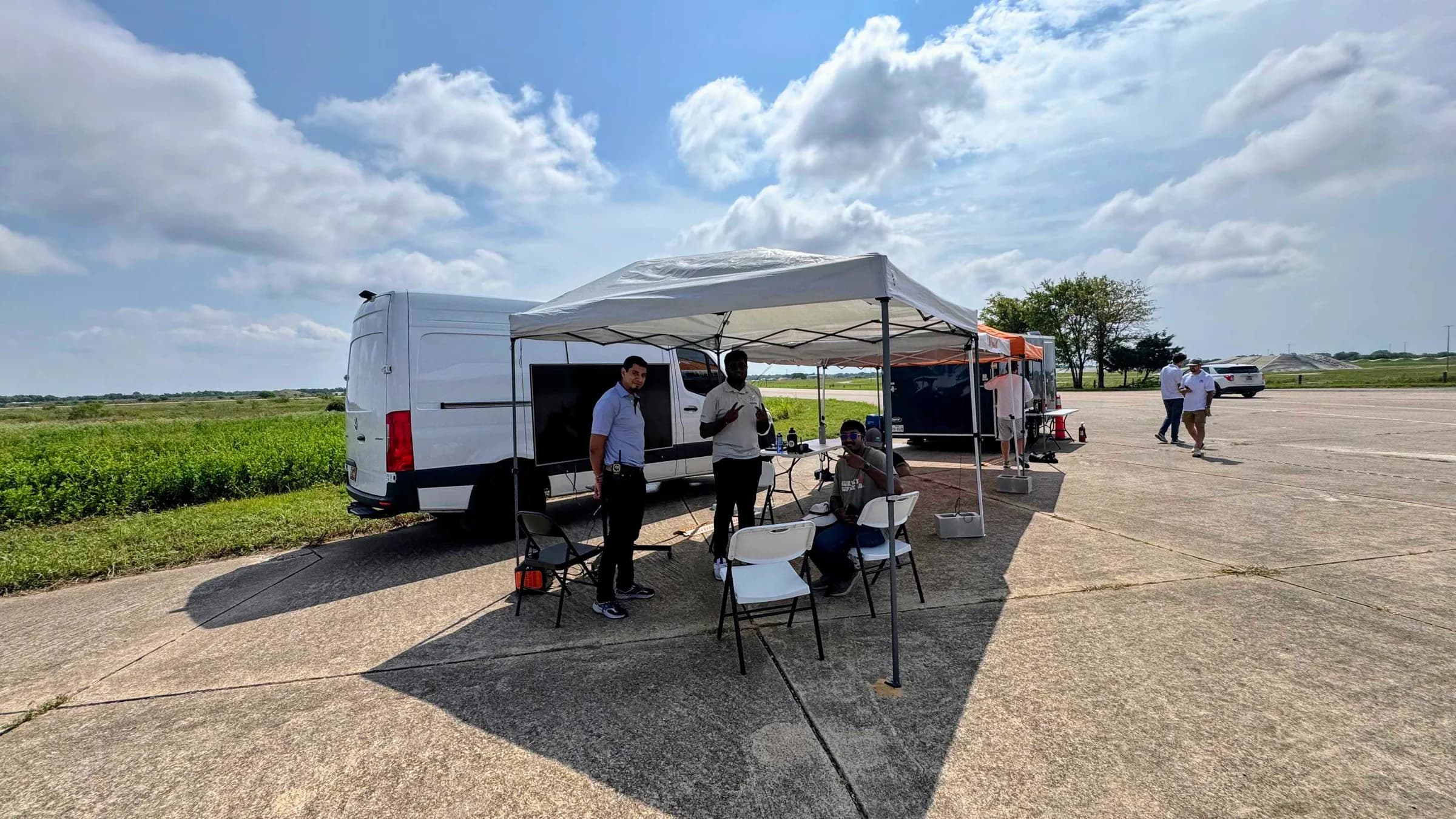 The Cacti team at an outdoor field test, working under a canopy beside a support van on an airfield runway